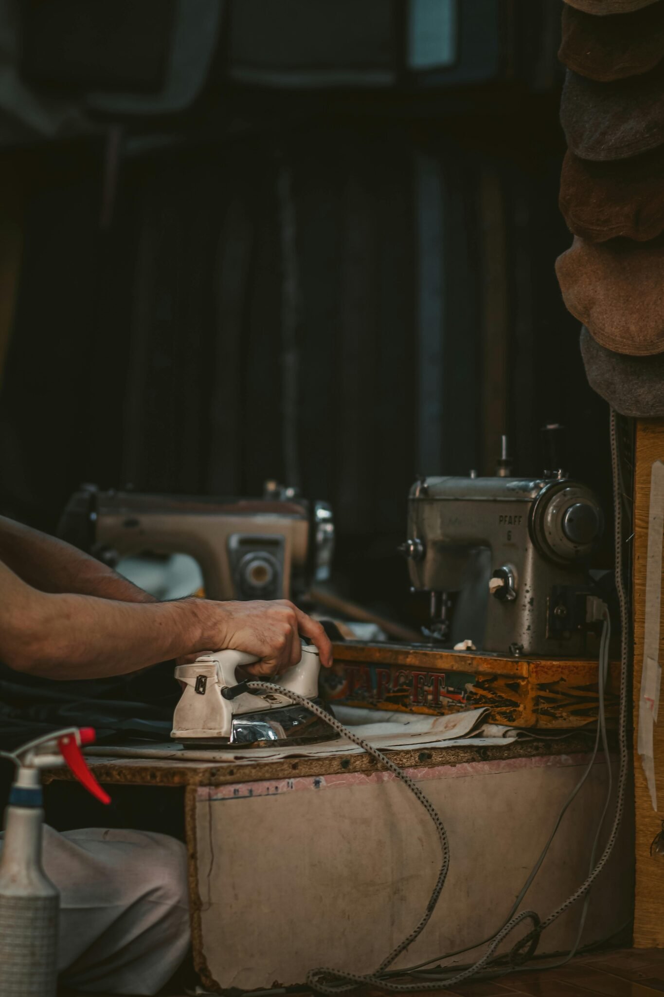 A vintage sewing station shows a person pressing clothes beside an old sewing machine.